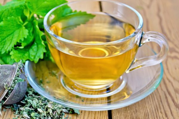Herbal tea in a glass cup, metal sieve with dry mint leaves, fresh mint leaves on the background of wooden boards