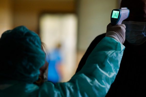 Otopeni, Romania - February 25, 2020: A woman in a protective suit measures the temperature of a man inside the Henri Coanda International airport for coronavirus symptoms.