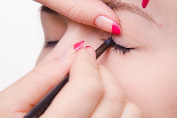 Makeup artist paints eyelashes of a beautiful young girl in the makeup