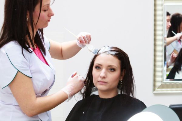 Professional female hairdresser applying color to female customer at design hair salon, woman having her hair dyed, Hair dye colouring in process