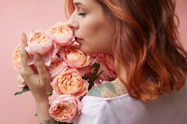 Beautiful girl with fragrant flowers on a background in a trendy color of the year 2019 Living Coral Pantone. Mother's Day and Valentine's Day greeting post cards.