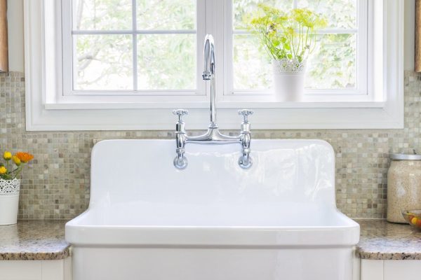 Kitchen interior with large rustic white porcelain sink and granite stone countertop under sunny window