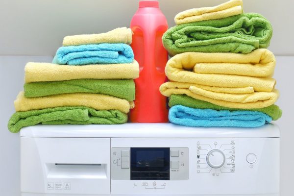 Pile of fresh colorful towels and bottle of detergent on washing machine