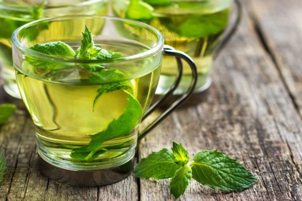 Hot mint tea in glass cup on wooden background, selective focus