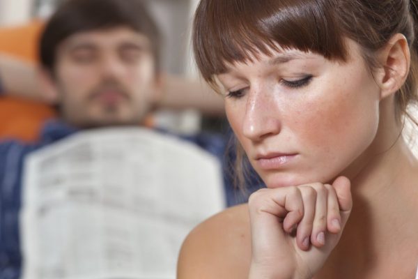 sad woman in front of sleeping man with newspaper