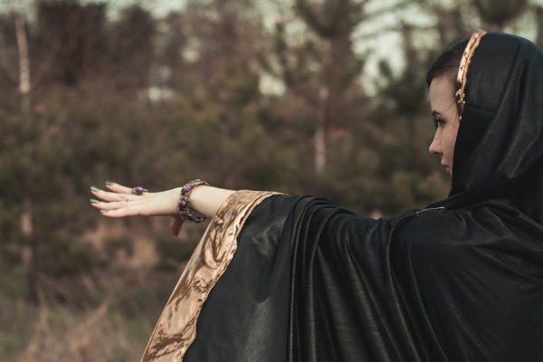 a young witch uses her magic in a black robe with a hood in the forest