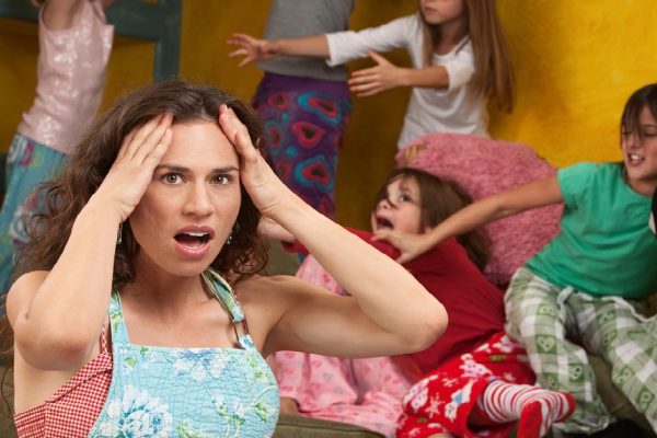 Upset mother with hands on head among mischievous little girls