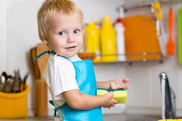 Little boy washing dishes in domestic kitchen