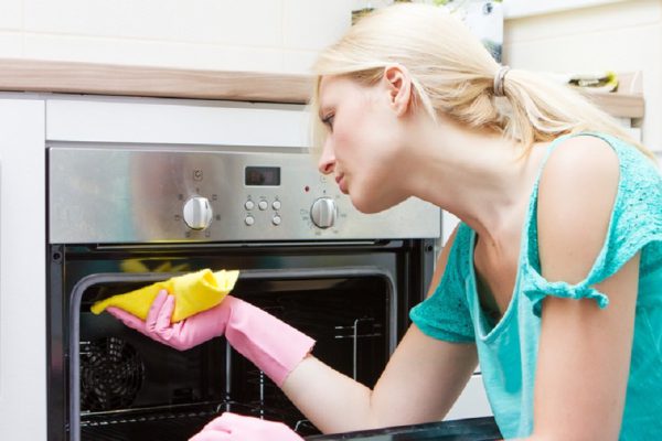 Young woman cleaning oven in the kitchen.