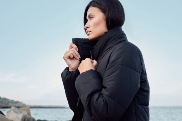 Side view of gorgeous Asian brunette girl in down jacket intently looking away on seaside