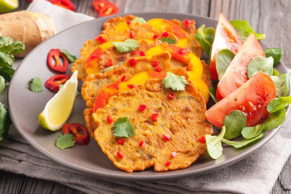 Indian chickpea crepes Pudla served on a plate with tomatoes, lime, cilantro, mash (mung bean) salad, chilli, ginger, bell pepper. Copy space.