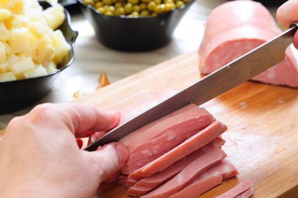 Preparing russian traditional salad Olivier, chopping sausage