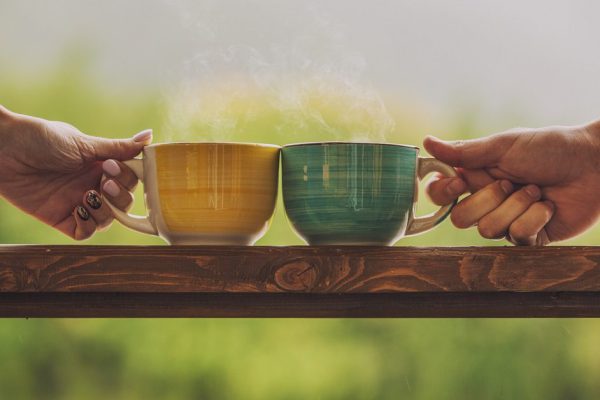 Hands holding mug with hot beverage, with tea on a wooden stand outdoors in the countryside