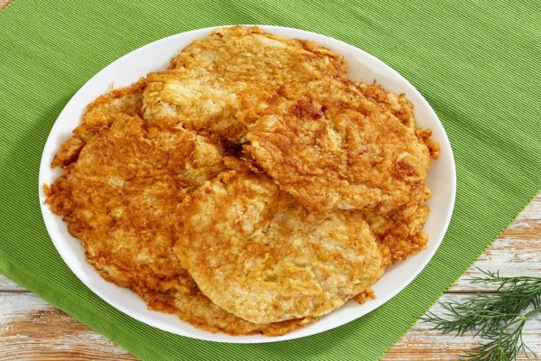 delicious pan fried in batter breaded boneless Pork Chops on white dish on table mat on old wooden planks, classic recipe, view from above
