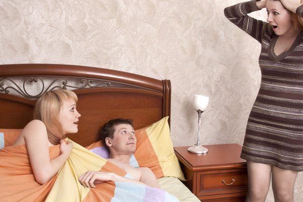 Couple in bed while an angry woman stand next to the bed. Love is over