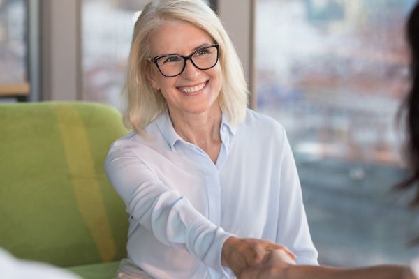 Smiling confident old mature woman job seeker applicant handshaking hr making good first impression at interview meeting, happy satisfied middle aged businesswoman shaking hand getting hired concept