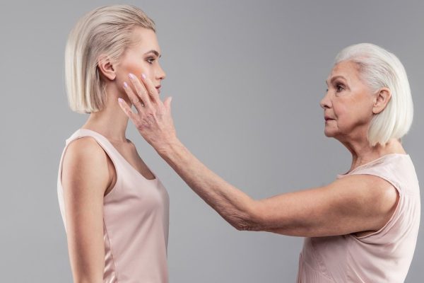 Standing together. Serious tidy senior lady petting her short-haired young version while looking directly into eyes