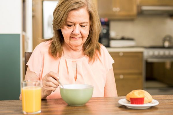 Pretty senior woman sitting in the kitchen and without appetite for breakfast