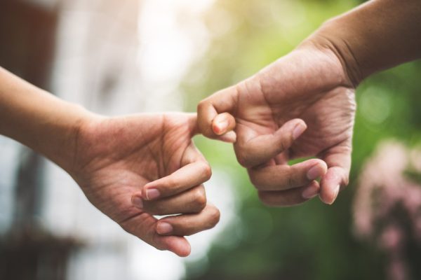 Close up couple holding pinkies fingers  in park in autumn as swear and promise gesture in wedding ceremony. Hands holding of love Valentines day theme. Togetherness of friendship with green natural