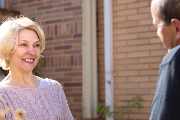 Mature couple having a conversation on a terrace: retired woman is holding her gardening tools and man holds a cup of water