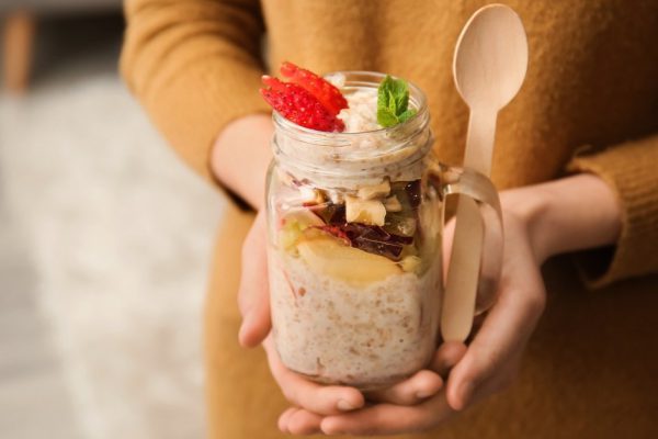 Young woman with tasty sweet oatmeal in mason jar, closeup