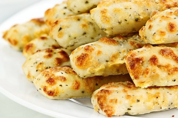 Fresh golden, cheesy breadsticks with marinara sauce and parmesan cheese in background. Shallow depth of field.