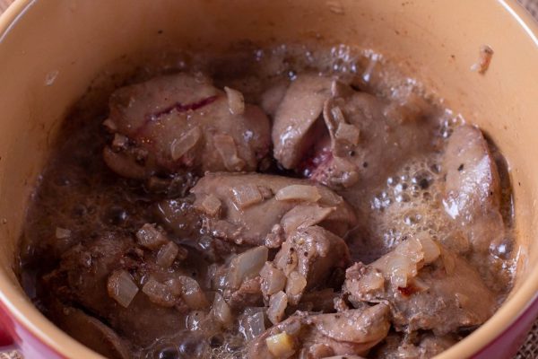 Chicken liver stew with vegetables in a pan on a wooden table