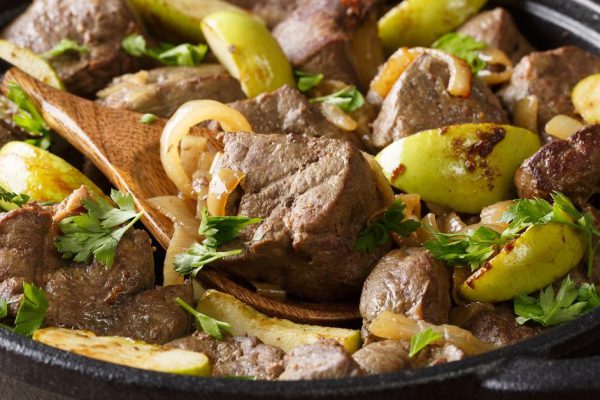 Spicy fried beef liver with apples and onions close-up in a pan on the table. horizontal