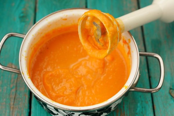 Tasty creamy pumpkin soup mixed with blender in white pot on turquoise table closeup