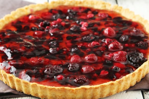 Fresh berry tart on white wooden background