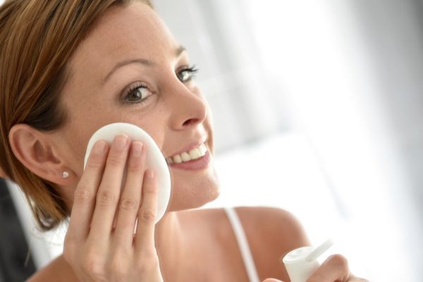 Woman in bathroom cleansing face in front of mirror