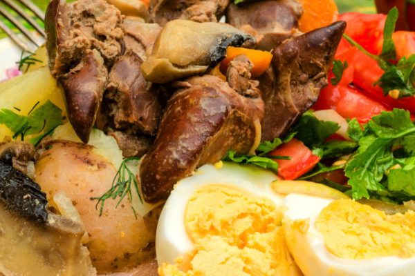 Fried chicken liver, chopped tomatoes with greens and boiled eggs on a white plate. Use for restaurant menu or dish description. The concept of delicious, quality food. Close-up.