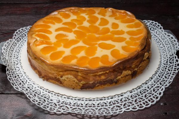 Cream cake with tangerines on mahogany wooden background.