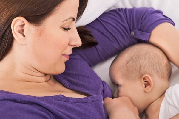 Smiling happy beautiful mother breastfeeding her baby infant