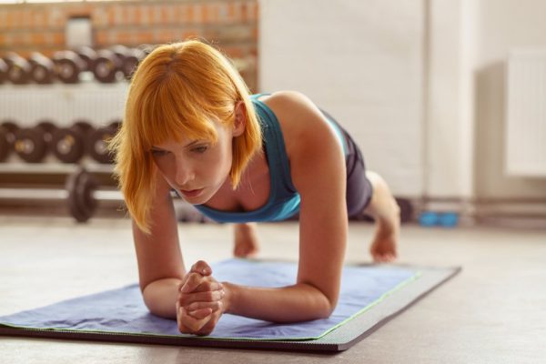 Young woman in the planking position on a gym mat with her body raised off the ground with a straight posture, low angle frontal view in a health and fitness concept