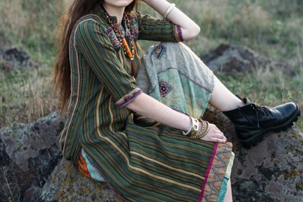 Beautiful hippie woman sitting on stone at sunset outdoors