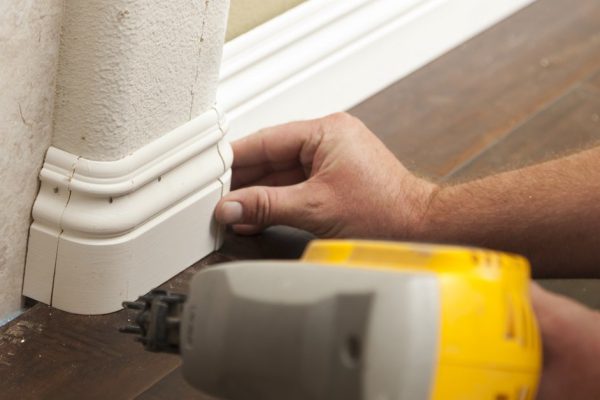Contractor Nailing New Baseboard with Bull Nose Corners and New Laminate Flooring Renovation Abstract.