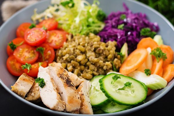 Healthy salad with chicken, tomatoes,  cucumber, lettuce, carrot, celery, red cabbage and  mung bean on dark background. Proper nutrition. Dietary menu.