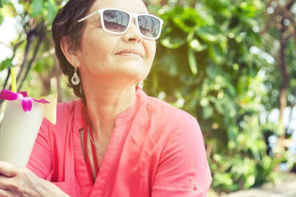 beautiful elderly woman in a hat with a cocktail in hand. Summer, vacation, holiday, active retired people