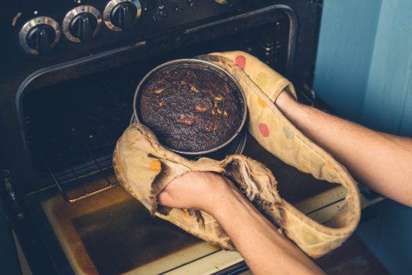 The hands of a man is removing a burnt cake from the oven