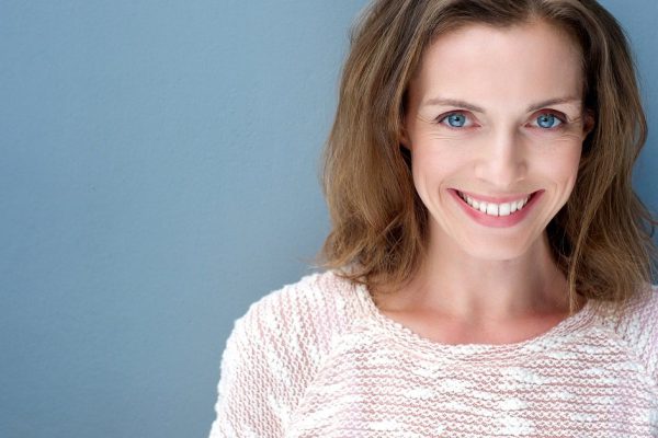 Close up portrait of a beautiful older woman smiling with sweater on blue background