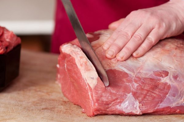 Closeup of the hands of a butcher cutting slices of raw meat off a large loin