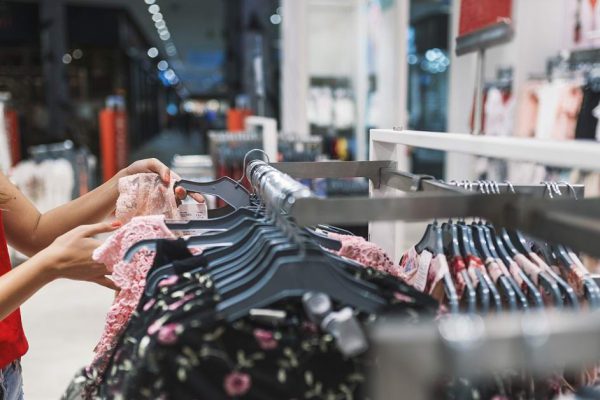 Young woman choosing clothes on a rack in a showroom.  Beautiful woman shopping trendy clothes. Shopaholic woman shopping clothes on sale. shopping, fashion, style and people concept