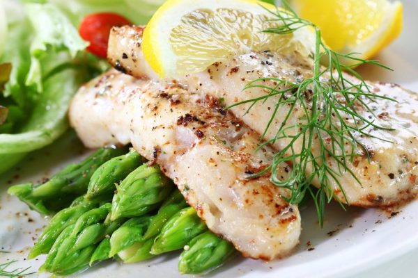 Delicious fried fish on green asparagus with salad