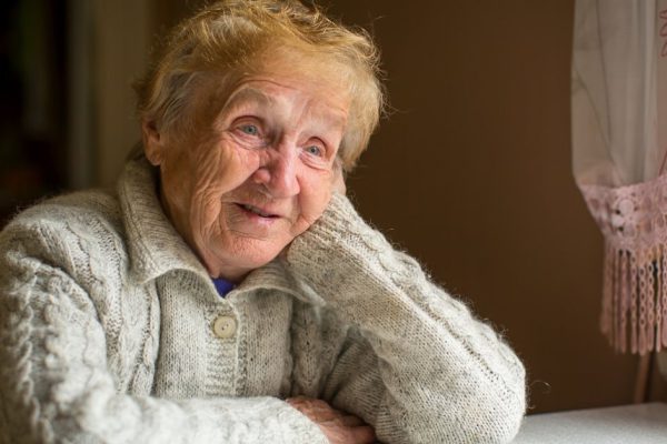 An elderly woman sits at a table near the window.