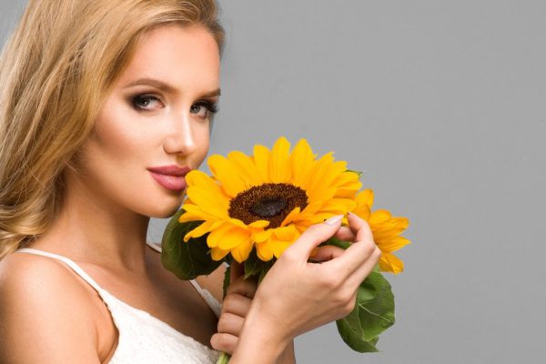 Portrait of attractive summer woman with sunflower in hand on blue background