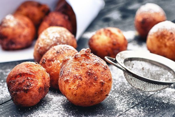Fresh fried donuts with powdered sugar on black wooden table