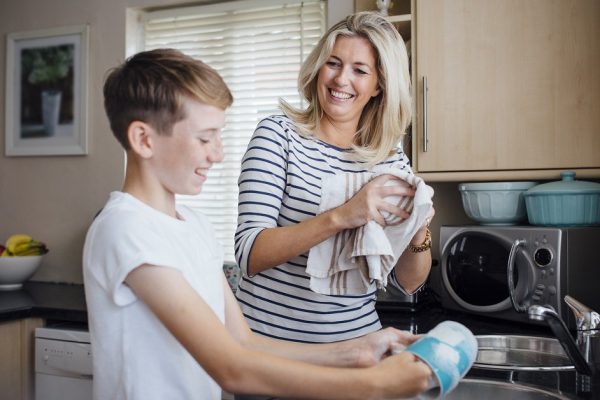 Mother and son doing the dishes together. They are talking and laughing as the boy washes and the mother dries dishes.