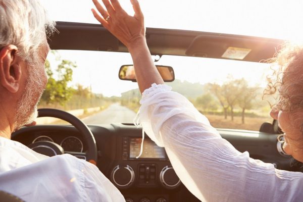 Mature Couple Driving Along Country Road In Open Top Car