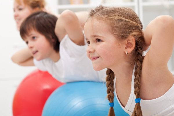Kids and woman doing gymnastic exercises with balls - stretching their back